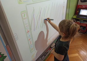 Dziewczynka rysuje na tablicy multimedialnej.